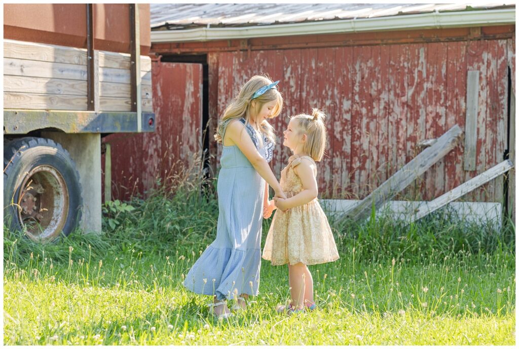 two girls holding hands and smiling at each other at a red barn