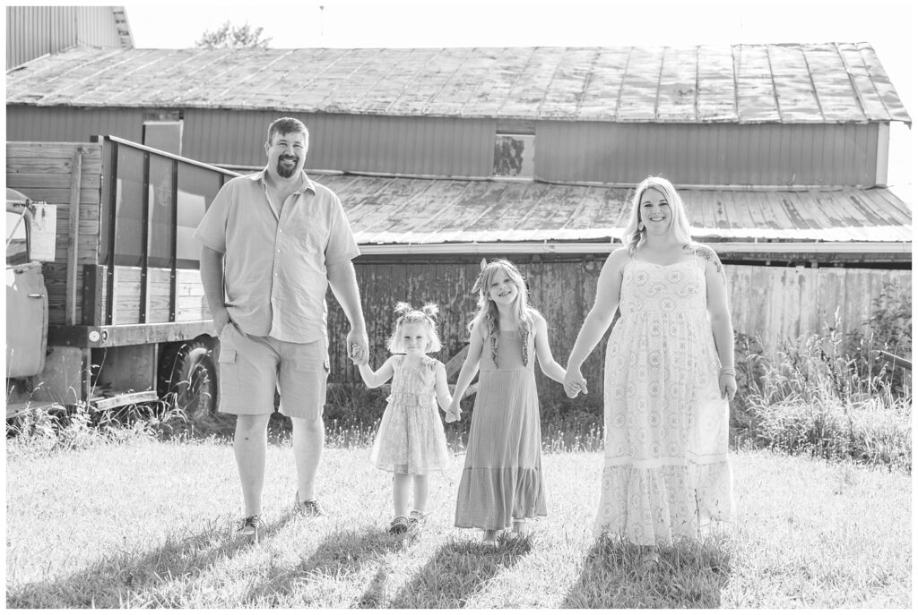 family holding hands and posing in front of a red barn at Tiffin, Ohio portrait session