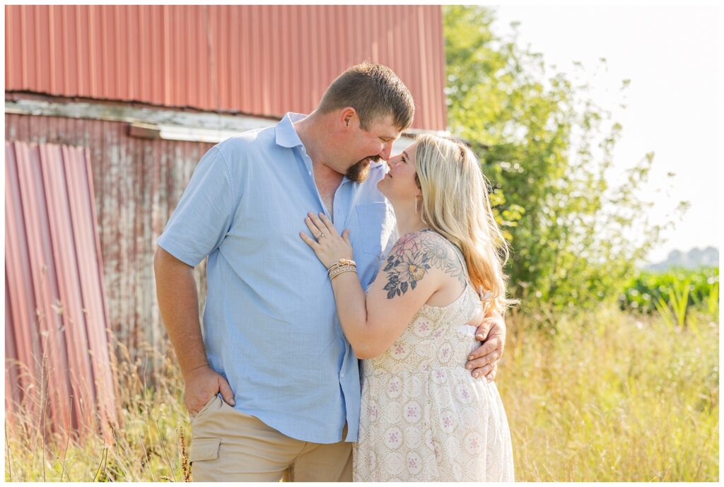mom and dad holding each other and touching noses in front of a red barn