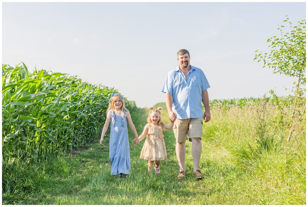 dad walking with his daughters in the grass next to a corn field for Fremont, Ohio family session