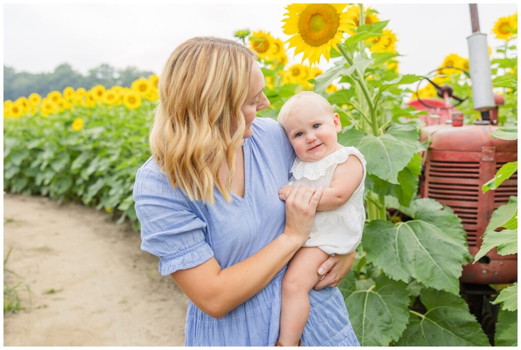 mom holding her daughter next to a red tractor and sunflowers in Lindsey, Ohio