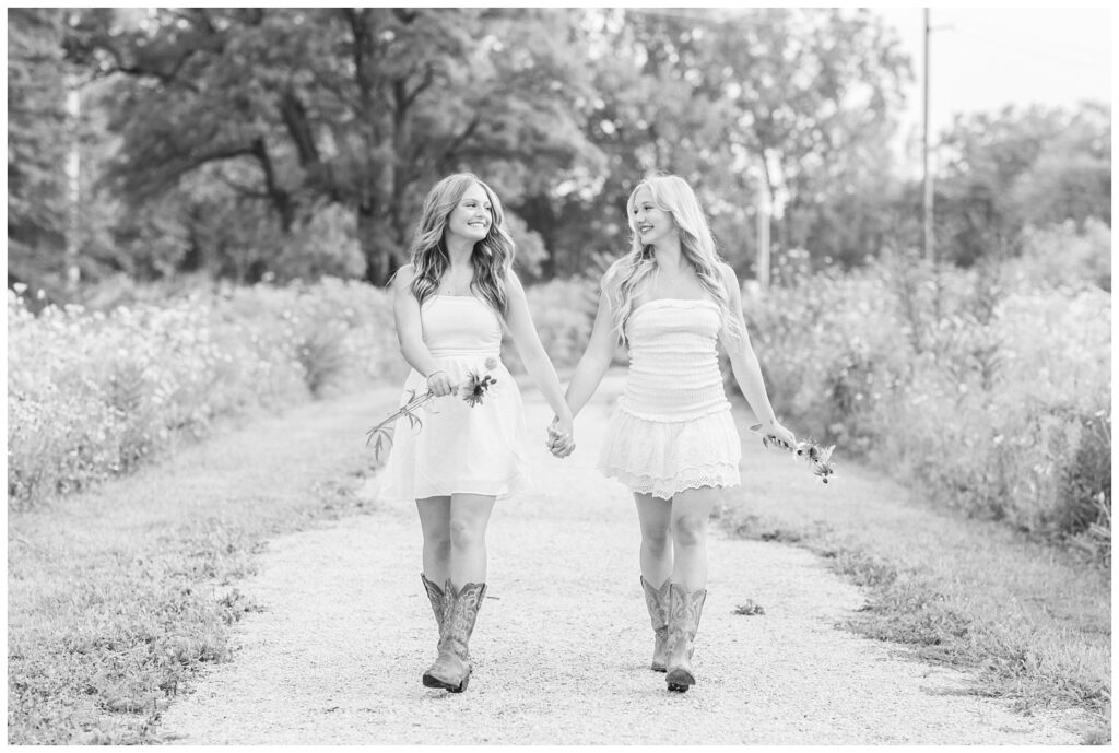 senior girls holding flowers and hands while walking in Don Miller Park