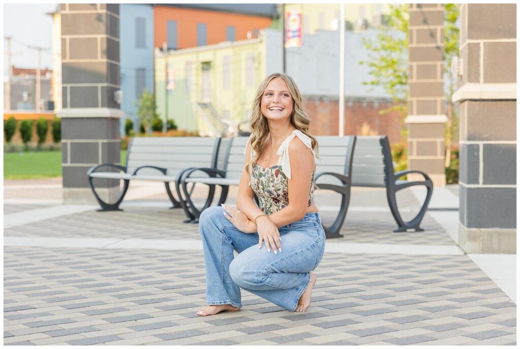 senior girl squatting while barefoot in downtown Fremont, Ohio park