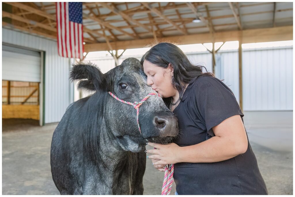 senior girl kissing her black and white cow inside a white barn
