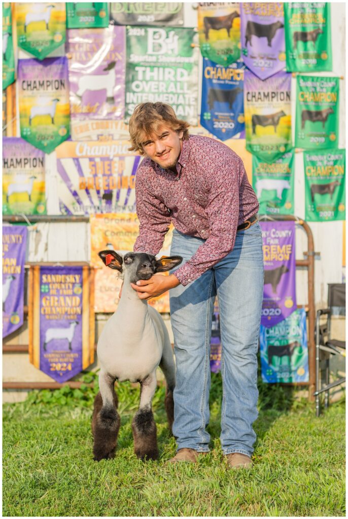 senior standing in front of his awards and holding a goat for photoshoot