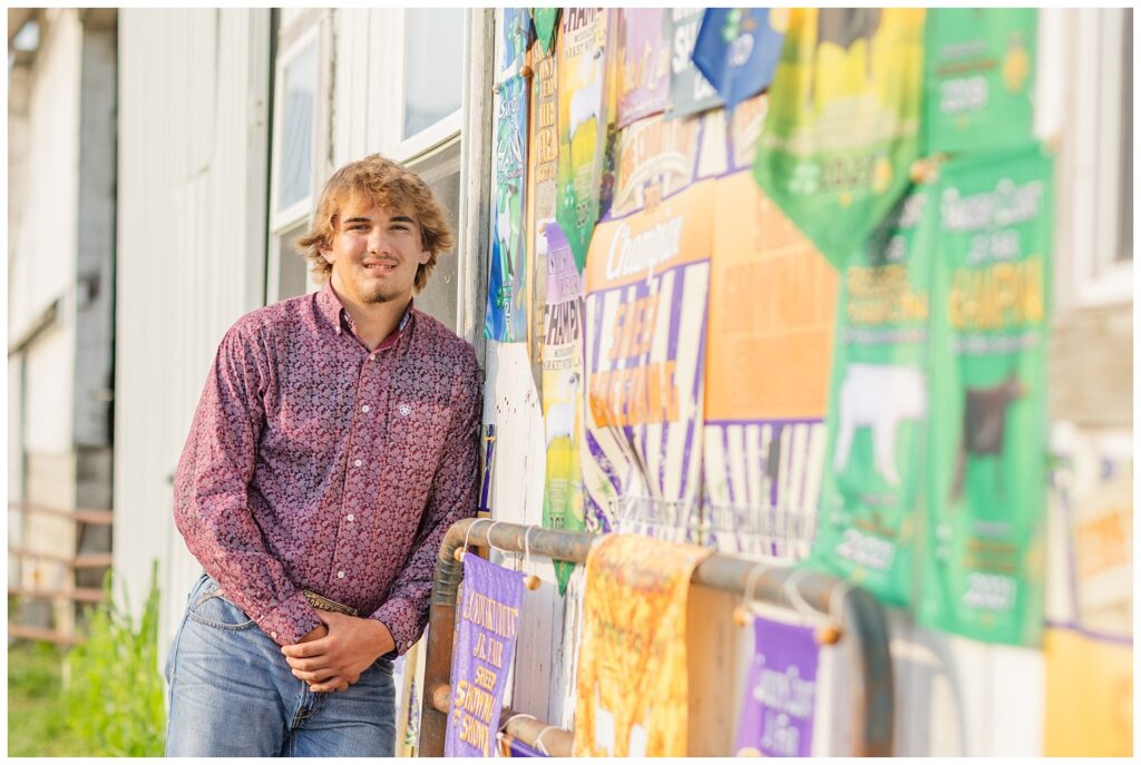 senior boy wearing red shirt and jeans posing in front of his FFA awards