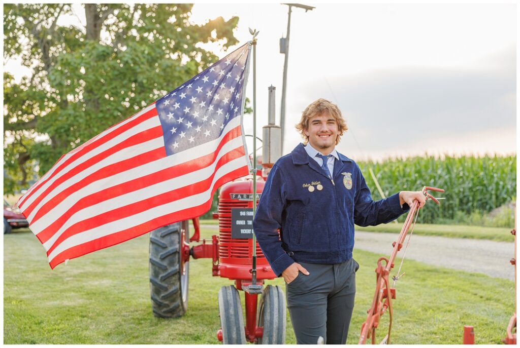 senior boy posing in front of his family's red tractor near a corn field