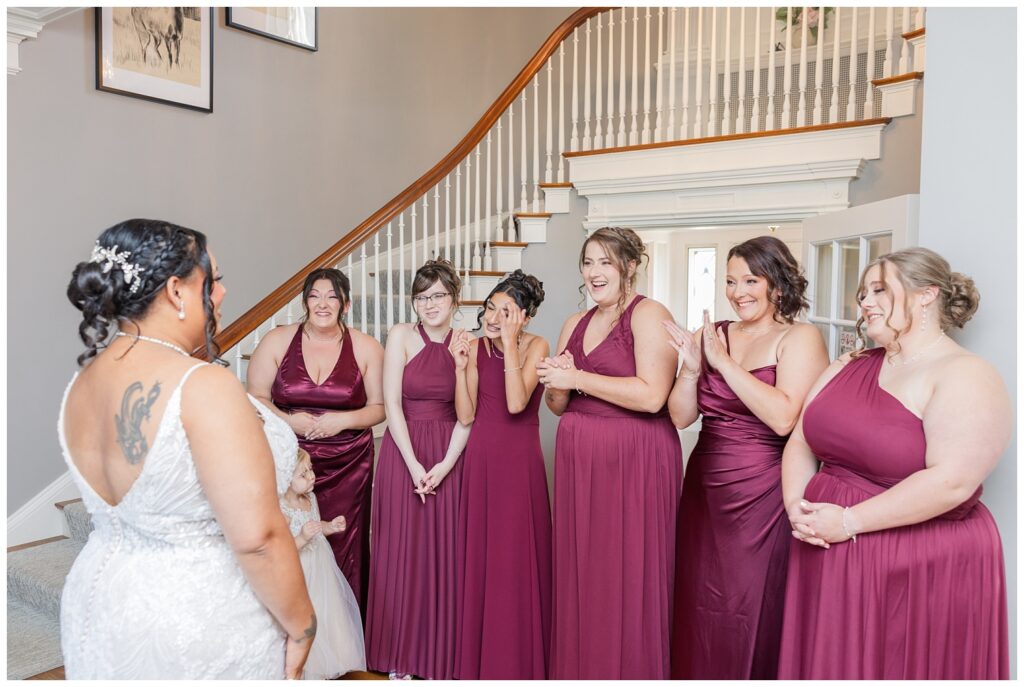 bridesmaids smiling at the bride as she reveals her dress in the foyer