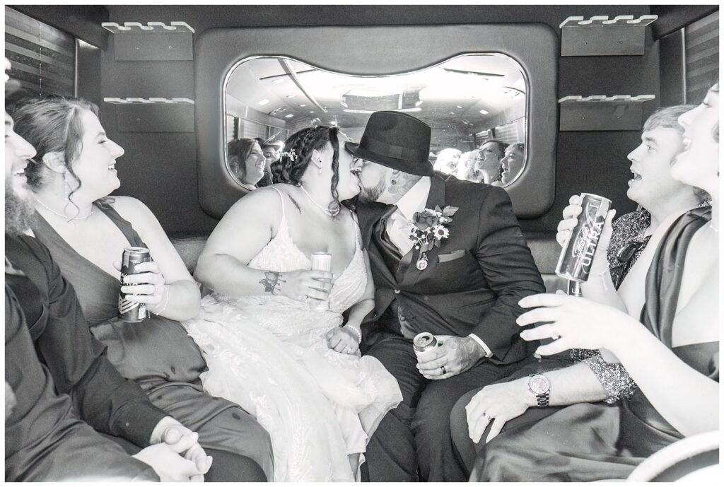 wedding couple sharing a kiss while holding a beer and riding in a party bus