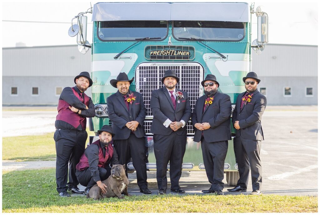 groom and groomsmen posing in front of the groom's blue green truck