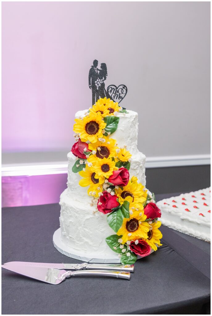 white wedding cake adorned with roses and sunflowers at the reception