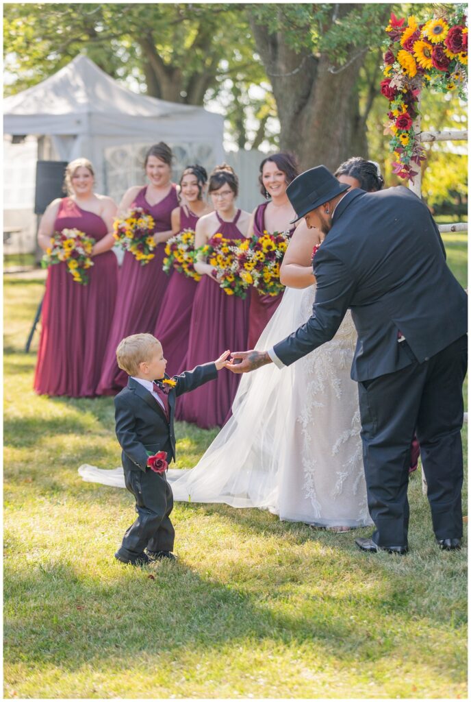 the ring bearer handing the rings to the groom during outside ceremony in Fremont, Ohio