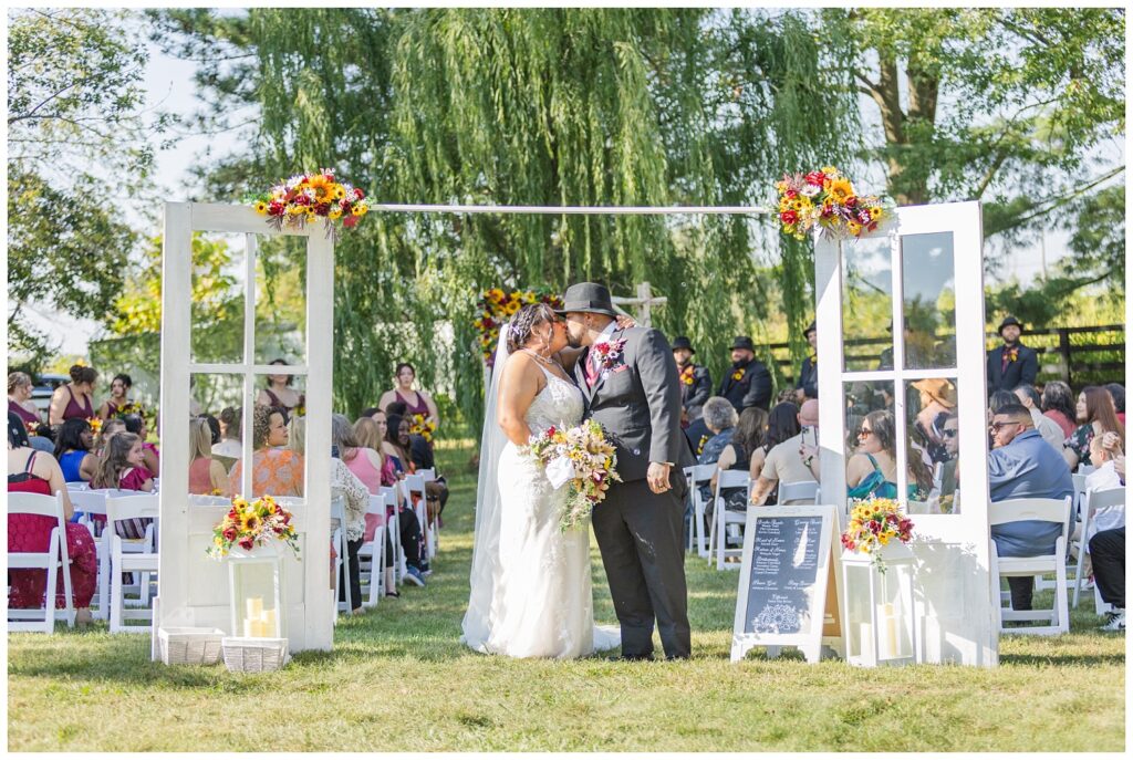 wedding couple share a kiss at the start of the aisle after outdoor ceremony