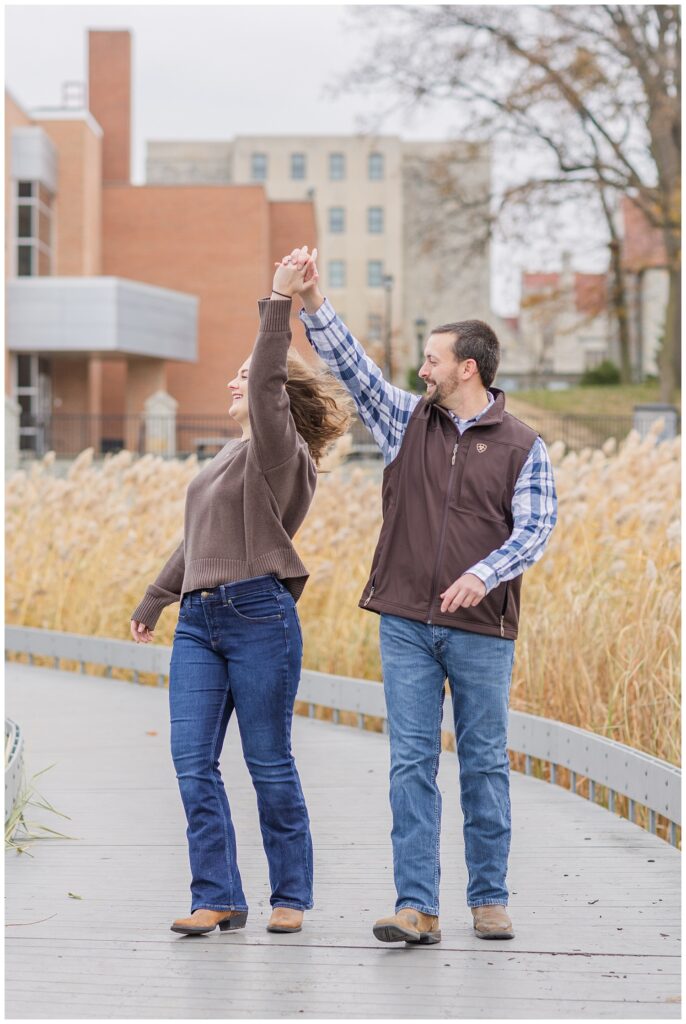 man spinning his fiancé around while posing on an outside walkway in Tiffin, Ohio