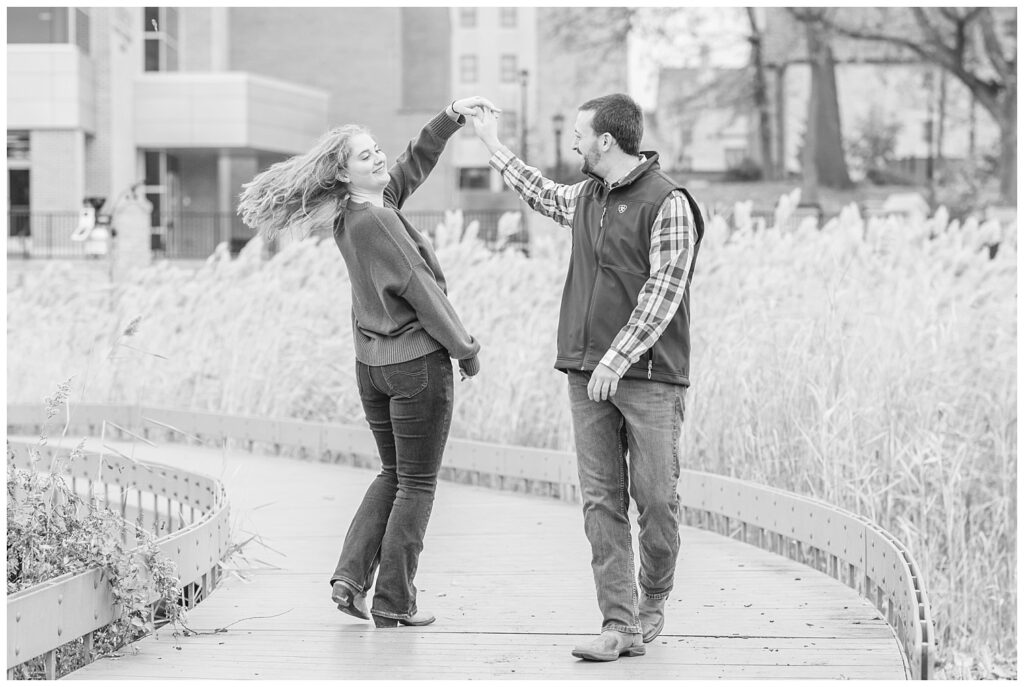 man twirling his fiancé around while posing on an outside walkway in Tiffin, Ohio
