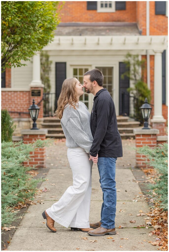 couple touching noses while posing in front of a white and brick house on campus in Tiffin, Ohio