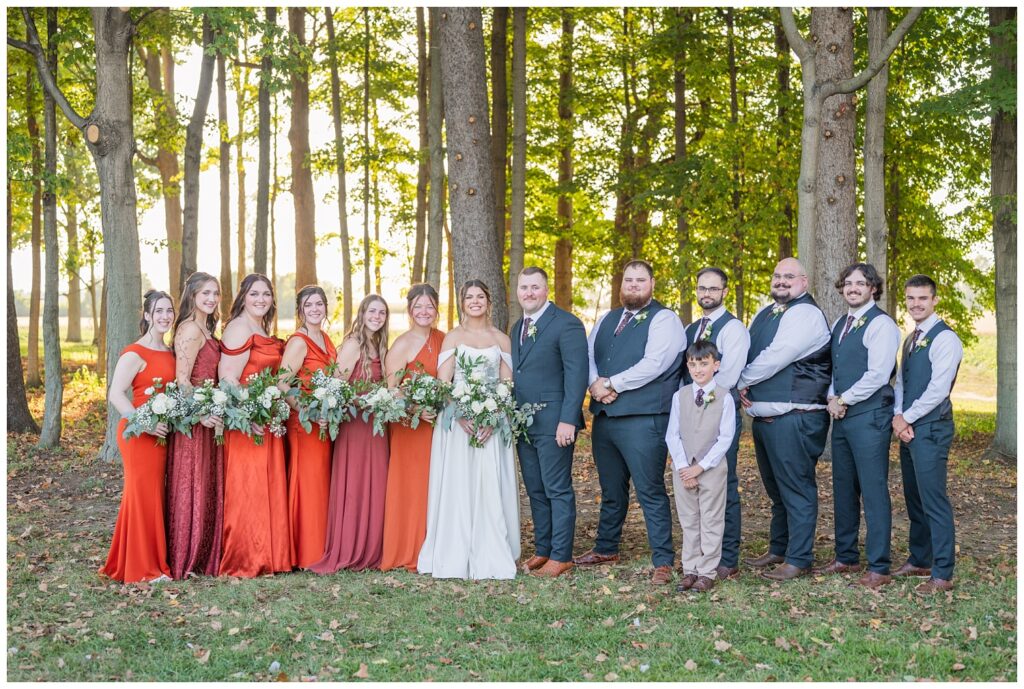 full wedding party posing in front of a row of trees outside at the Octagon House venue