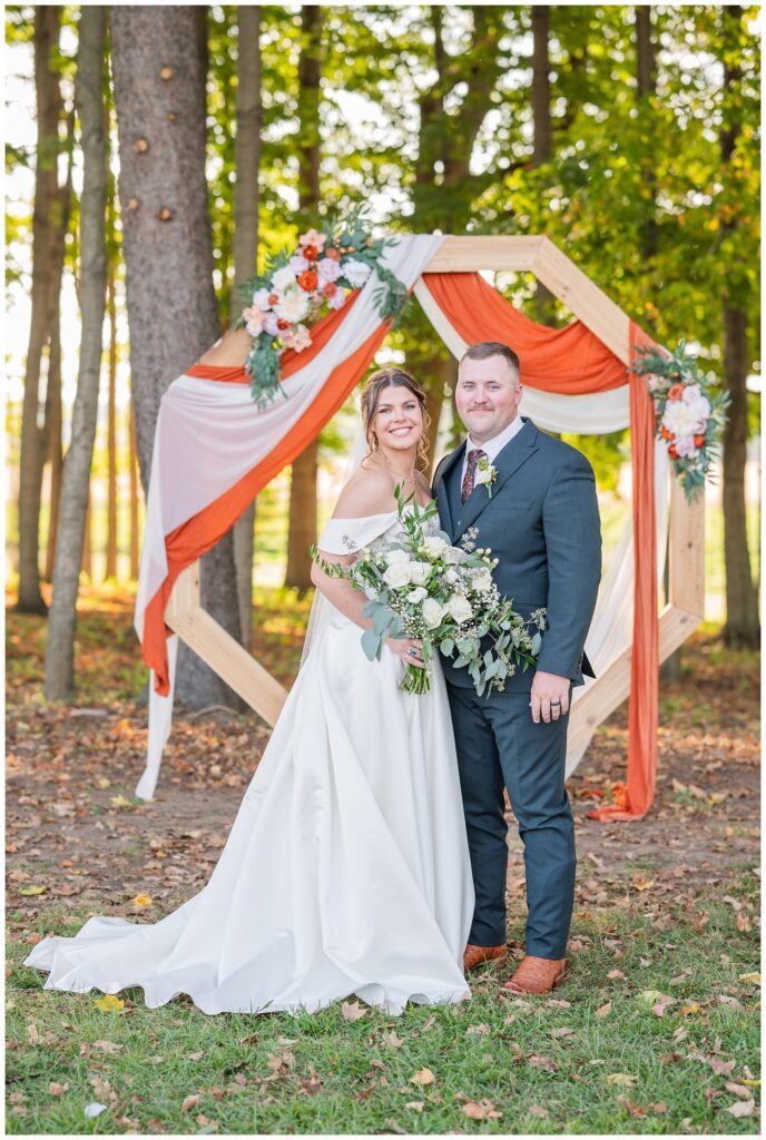 bride and groom posing in front of the decorated wood octagon at the wedding venue
