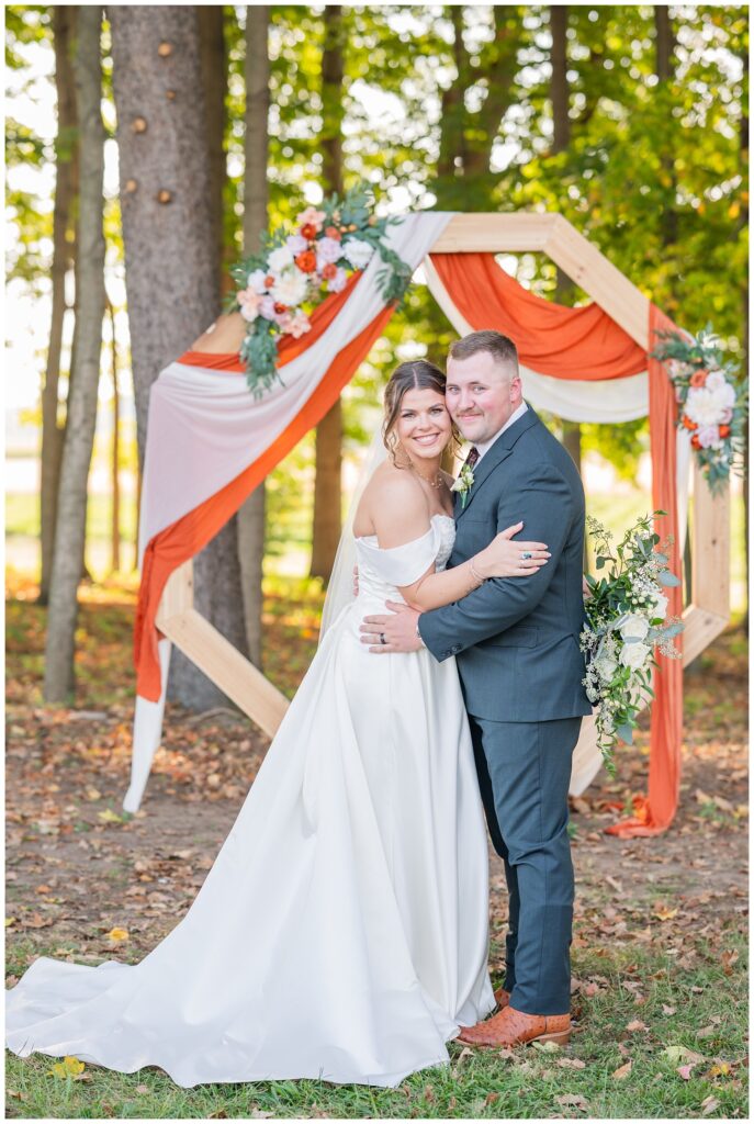 wedding couple holding each other in front of the decorated octagon at outdoor venue