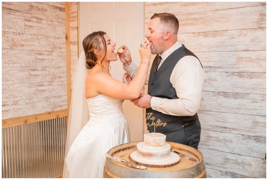 wedding couple if Tiffin, Ohio feeding each other cake sitting on a wooden barrel