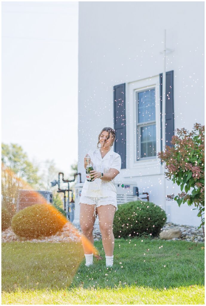 bride popping a bottle of champagne in front of the wedding venue outside
