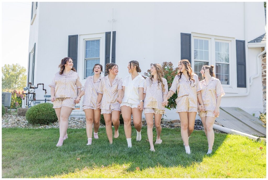 bridal party holding hands and laughing in their pajamas outside the venue