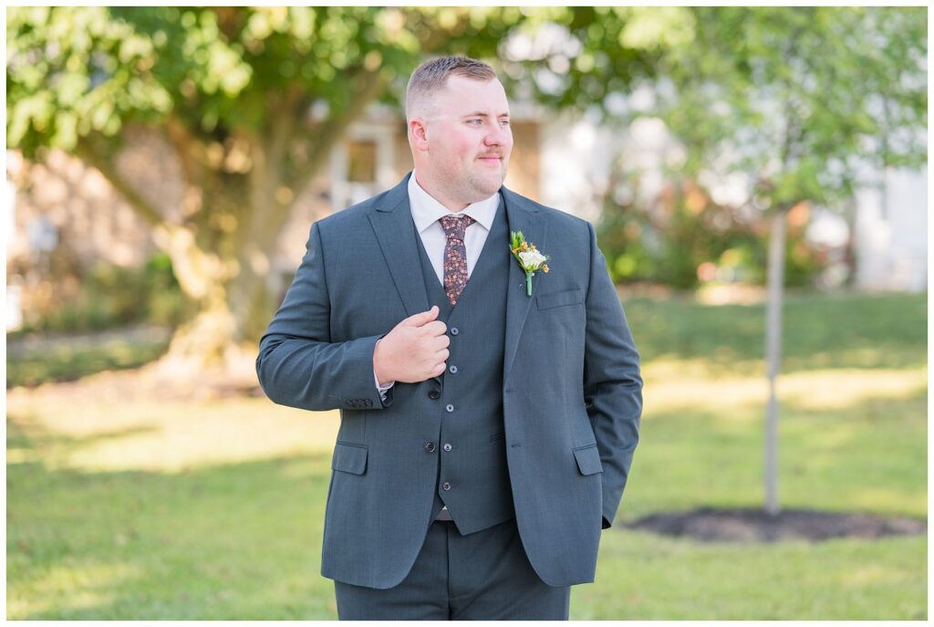groom wearing a dark gray suit and posing with his hand on jacket outside