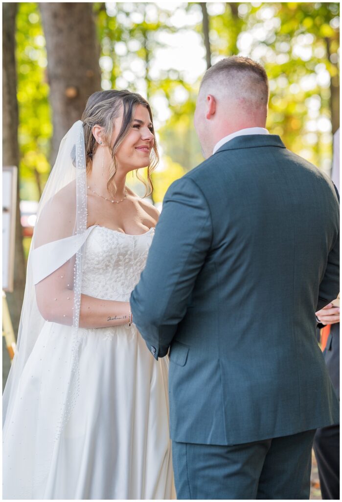 bride smiling at the groom while he says his vows outdoors at Tiffin, Ohio wedding venue