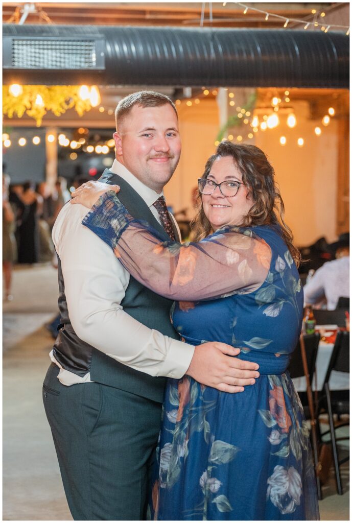 groom and his mom smiling while sharing a dance in the barn reception