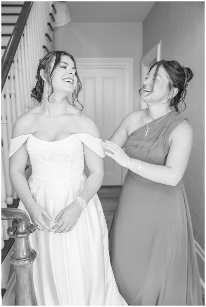 maid of honor laughing with the bride while she gets into her dress