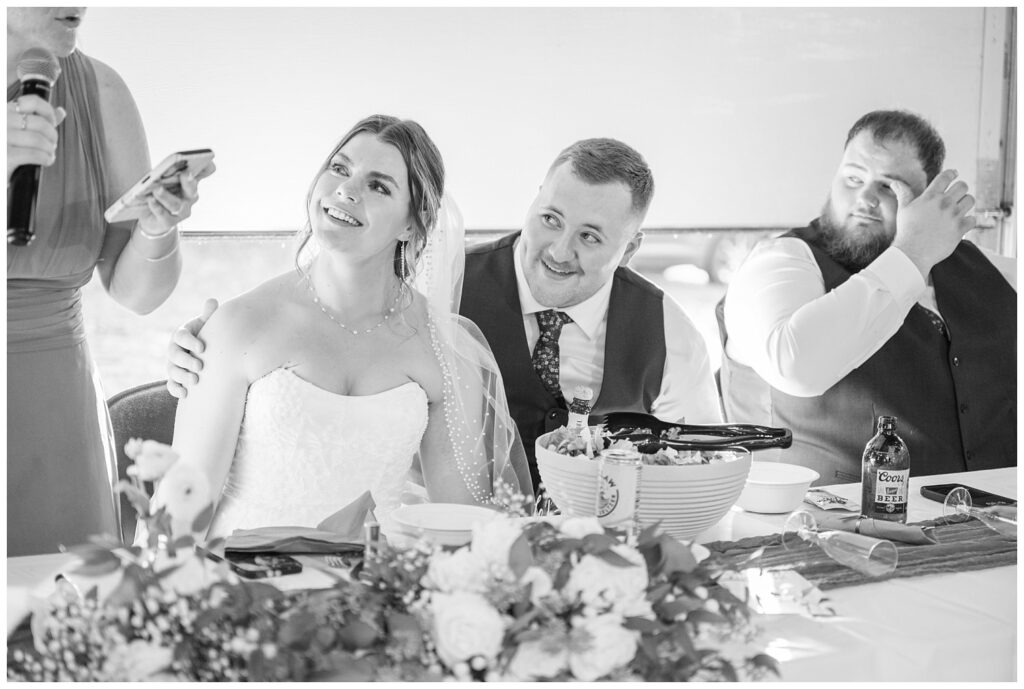 bride and groom smiling on as they watch the maid of honor give a speech