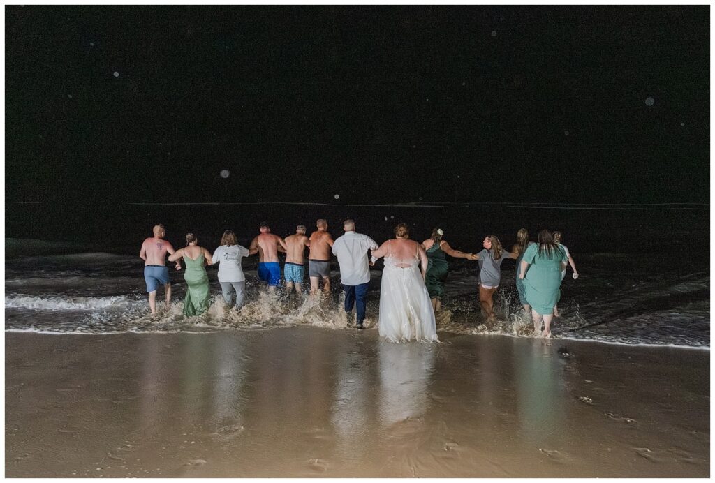 bride and groom along with friends walking in to the ocean at night after Punta Cana reception