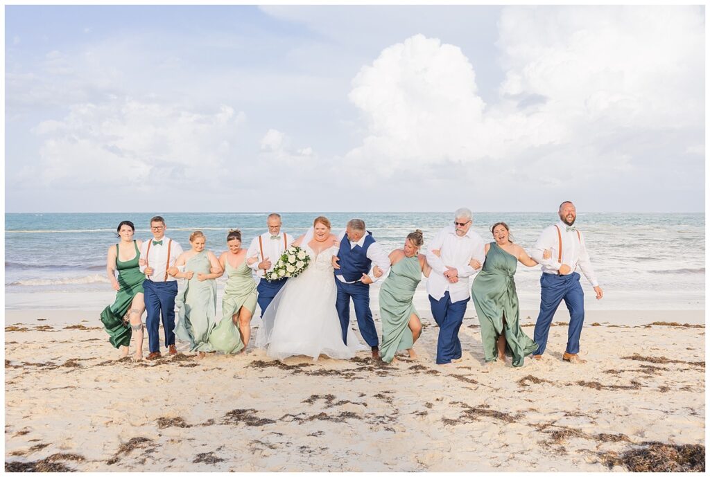 full wedding party walking and hitting hips together on the beach at the ocean at Punta Cana Dreams Resort