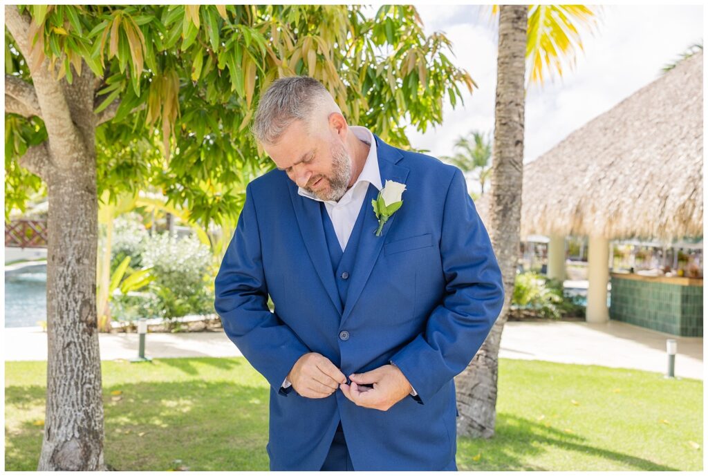 groom adjusting his jacket buttons wearing a blue suit near the pool area in Punta Cana