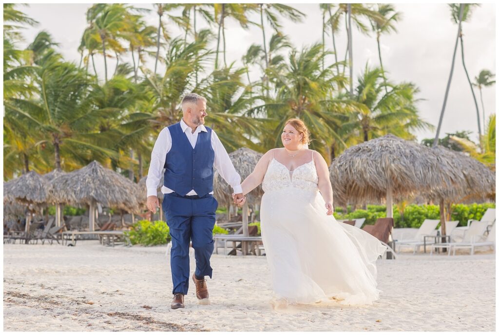 bride and groom holding hands on the beach among palm trees for fall destination wedding in Punta Cana