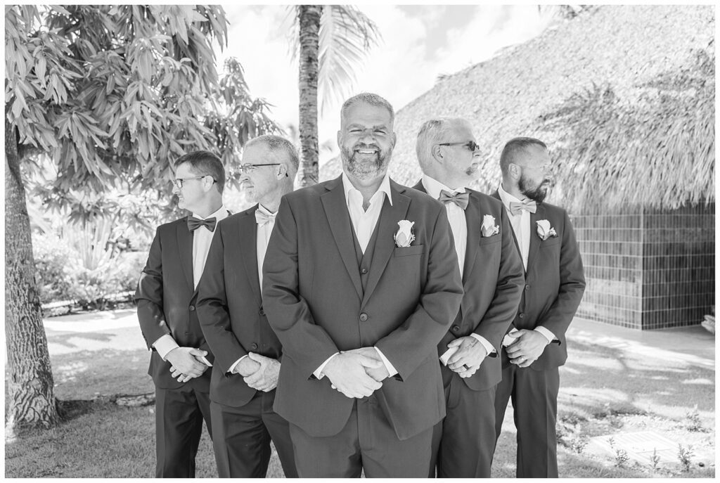 groomsmen posing together in a group while the groom smiles at the photographer