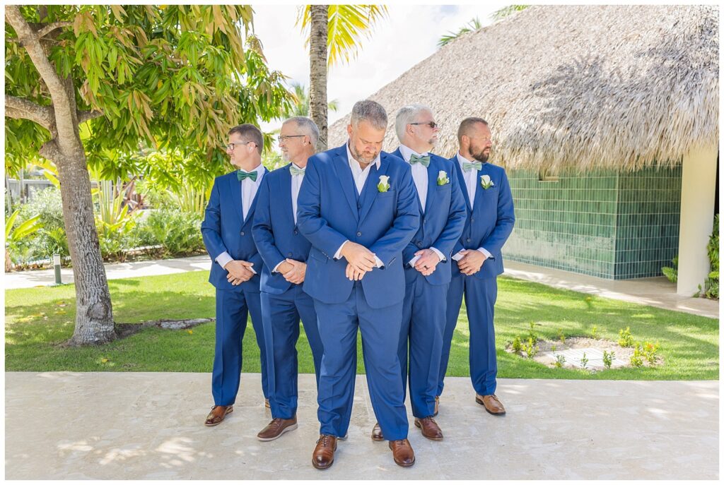 groomsmen posing together in a group while the groom looks at his watch