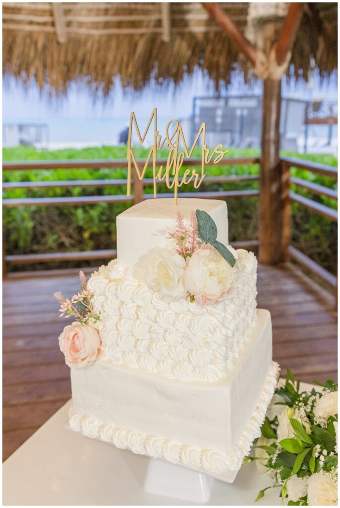 three layered square cake with pink and white roses sitting on a table for Punta Cana wedding reception