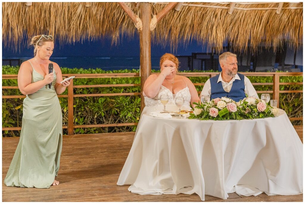 maid of honor giving the toast while bride and groom look on from their sweetheart table 