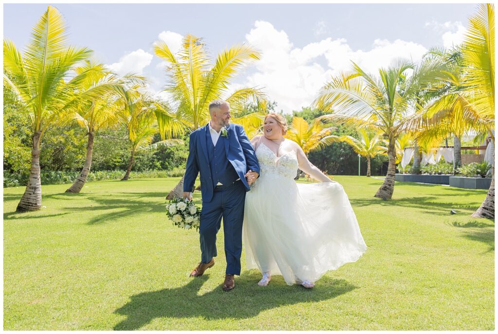 wedding couple bumping hips while walking together around palm trees at resort wedding 