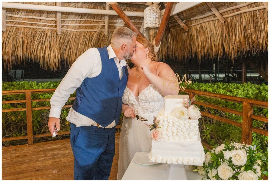 wedding couple kissing and cutting their cake on white table at Punta Cana wedding reception