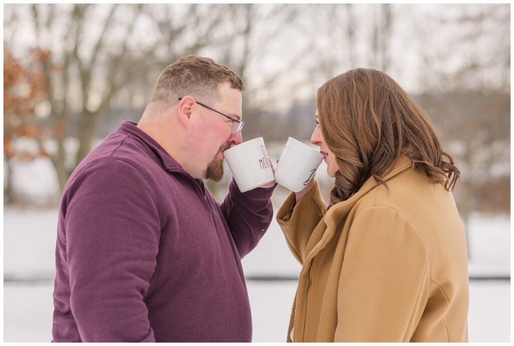 engagement session couple posing in the snow and drinking from white coffee mugs