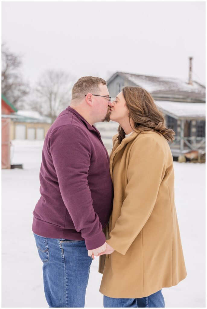 couple holding hands and kissing in the snow at nature preserve in Bloomville, OH