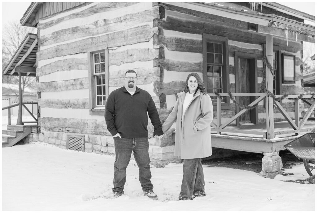 engaged couple posing in the snow in front of a log cabin in Bloomville, OH