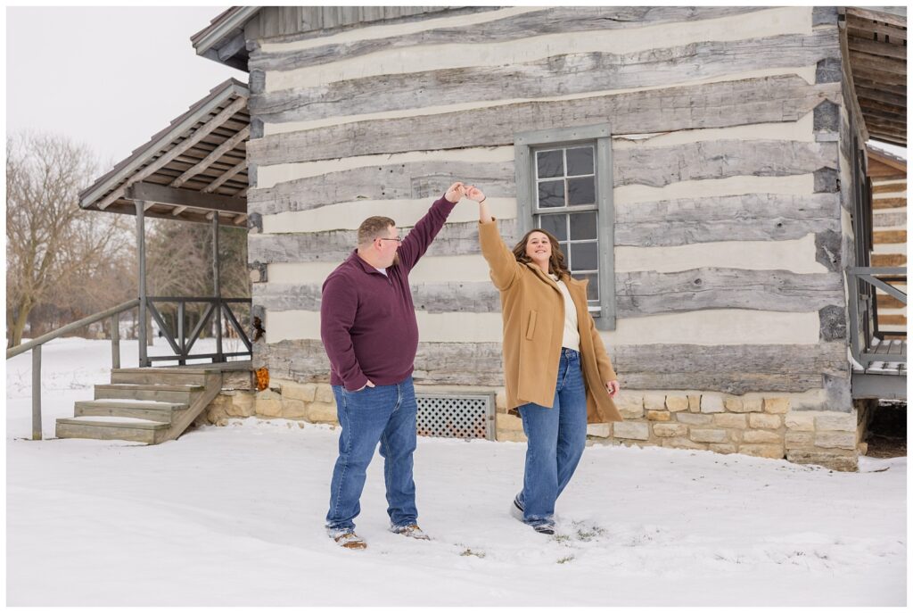 couple twirling in the snow in front of a log cabin with Bloomville, OH engagement photographer
