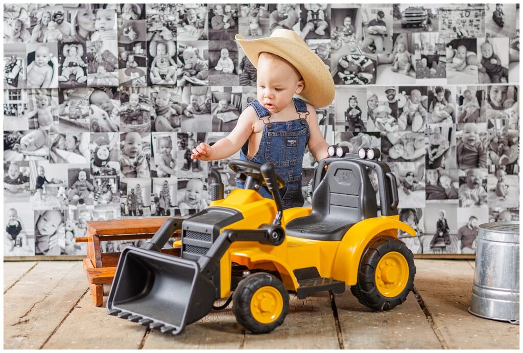 one year old boy wearing overalls and a cowboy hat playing with a kid's black and yellow tractor
