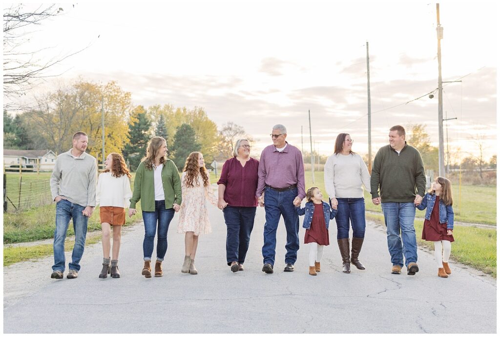 three generations holding hands and walking on a road for extended family session at golden hour
