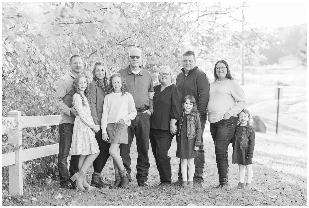 three generations holding hands and posing against a white fence for extended family session at golden hour