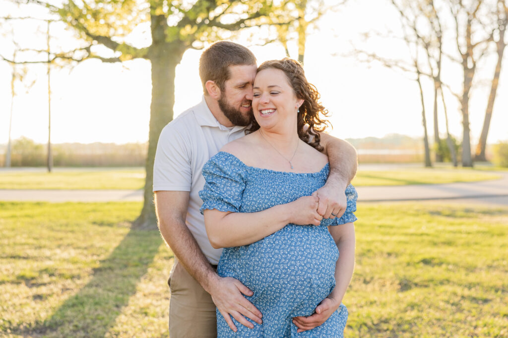 husband hugging his wife from behind to show her baby bump at Lake Erie maternity session