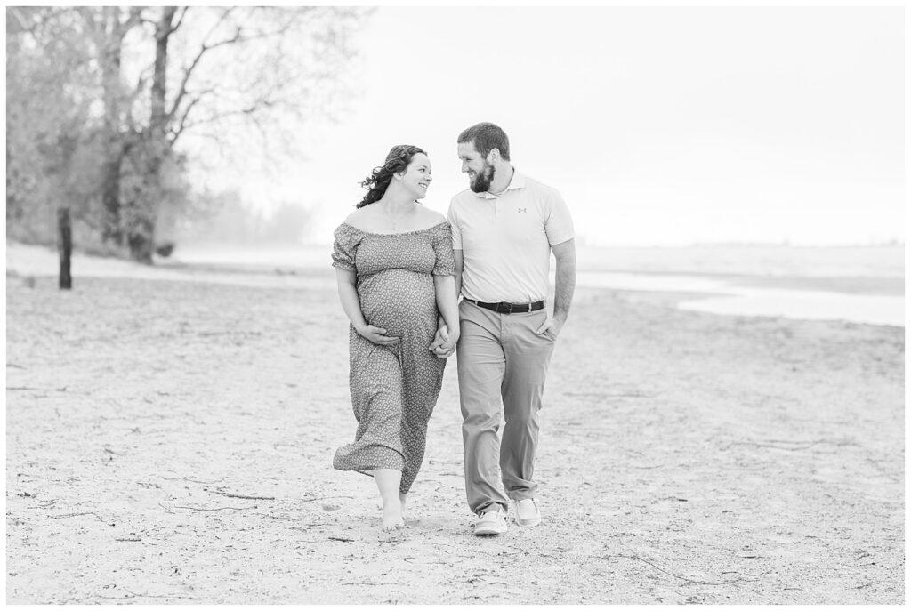 husband and wife holding hands on the beach during maternity session at East Harbor State Park
